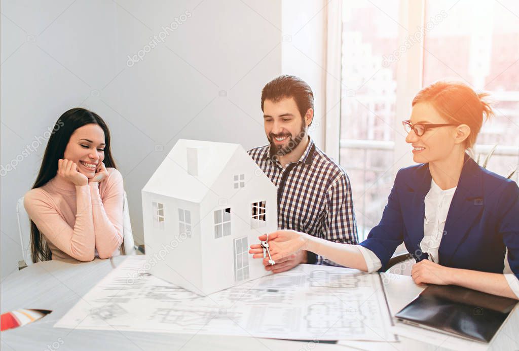 Young family couple purchase rent property real estate . Agent giving consultation to man and woman. Signing contract for buying house or flat or apartments. He holds a model of the house in hands