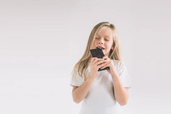 Kleines Kind beim Essen einer Schokoriegel. blondes Mädchen isoliert auf weißem Hintergrund. — Stockfoto