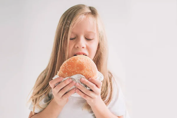 Niño sosteniendo un pedazo de hamburguesa. El chico come comida rápida. comida no útil. bebé muy hambriento. Chica aislada sobre fondo blanco . — Foto de Stock