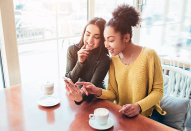 İki neşeli ve güzel kız birlikte masanın ve telefonda bir şey izliyor. Rahat ve mutlu görünüyorlar. Ayrıca kızlar birlikte harcama zaman tadını çıkarıyor