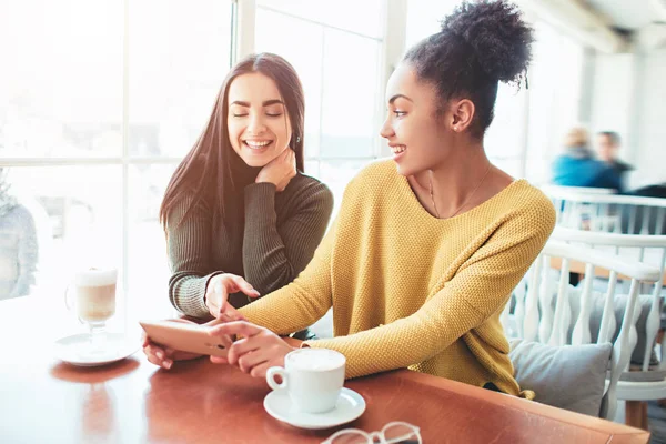 Zwei fröhliche und schöne Mädchen sitzen zusammen am Tisch und beobachten etwas am Telefon. Sie sehen entspannt und glücklich aus. Auch Mädchen genießen die gemeinsame Zeit — Stockfoto