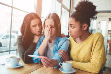 sarışın kız gösterir bir hamilelik testi test onun olumlu sonuç için tutuyor. Dissapointed, üzgün ve ağlamamak için zor görünüyor. İki en iyi arkadaşının ona destek için çalışıyoruz