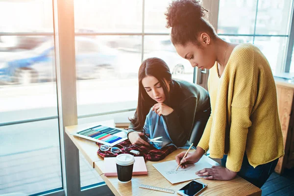 Dos mujeres jóvenes de pie juntas y trabajando para el mismo proyecto de moda. Están tratando de cortar una pieza de ropa y crear algo nuevo. Tienen algunas ideas sobre la futura colección de ropa. . — Foto de Stock