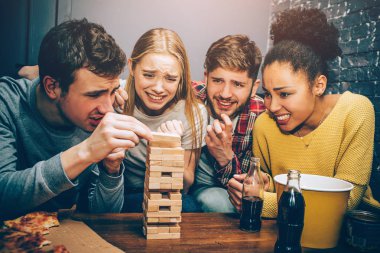 Dört grup Jenga oyunu oynarken. Yoğun ve sert oyundur. Bu havlu parçalarını çok yakında çocuk yüzünden sol tarafta düşmek gibi görünüyor.