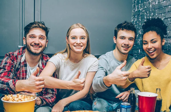 Närbild av fyra bästa vänner sitter tillsammans i ett litet rum och poserar för kameran. De visar sina tummar upp och leende. Tonåringar ser glad och nöjd. — Stockfoto