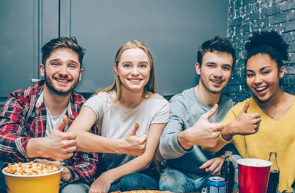 Nahaufnahme von vier besten Freunden, die zusammen in einem kleinen Raum sitzen und vor der Kamera posieren. Sie zeigen den Daumen nach oben und lächeln. Jugendliche sehen glücklich und zufrieden aus. — Stockfoto