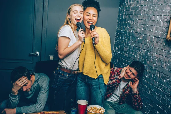 Deux filles chantent une chanson très fort. Leur petit ami ne l'aime pas parce que les jeunes femmes ne chantent pas très bien du tout. Donc les gars souffrent d'entendre de mauvaises voix — Photo