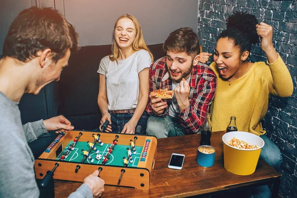 Ein Schuss, bei dem Jungen ein Brettspiel auf dem Tisch spielen, während Mädchen jubeln. Alle sind glücklich, nur an das Spiel zu denken. — Stockfoto