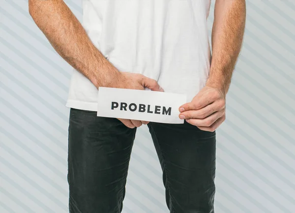 Ein Kerl, der Harn- oder Prostataprobleme hat, die wirklich schmerzhaft sind. junger Mann hält Zettel mit einem Schriftzug, auf dem das Problem steht. — Stockfoto