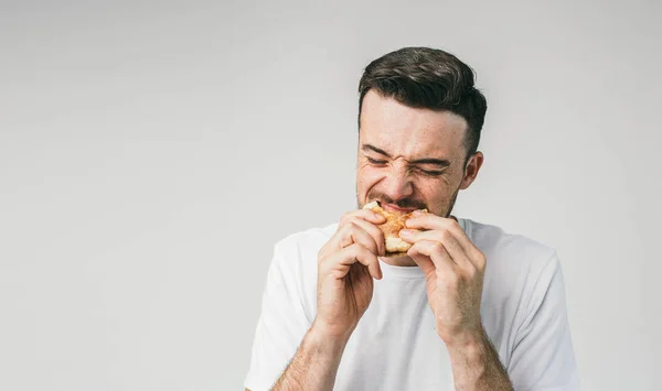 Nahaufnahme eines gutaussehenden Mannes, der in einen Burger beißt. Er beißt sehr hart zu. Der junge Mann erwartet, dass der Burger überhaupt nicht lecker sein wird. Schnitt-Ansicht. — Stockfoto