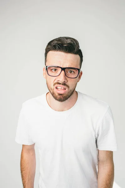 A portait of a guy in white t-shirt and glasses looking straight to camera. His sight is strange and disturbed. Close up. — Stock Photo, Image