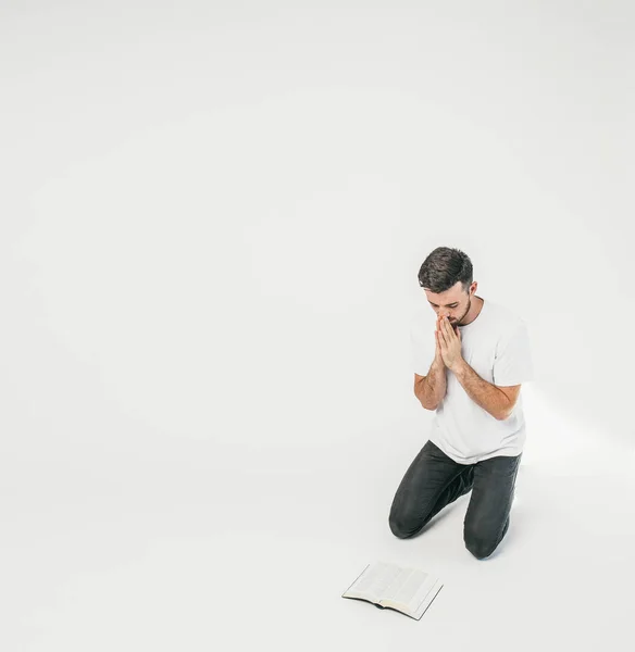 L'uomo adulto è in ginocchio e sta pregando mentre i suoi occhi guardano per terra. C'è una Bibbia davanti a lui. Questo tizio è un credente. . — Foto Stock