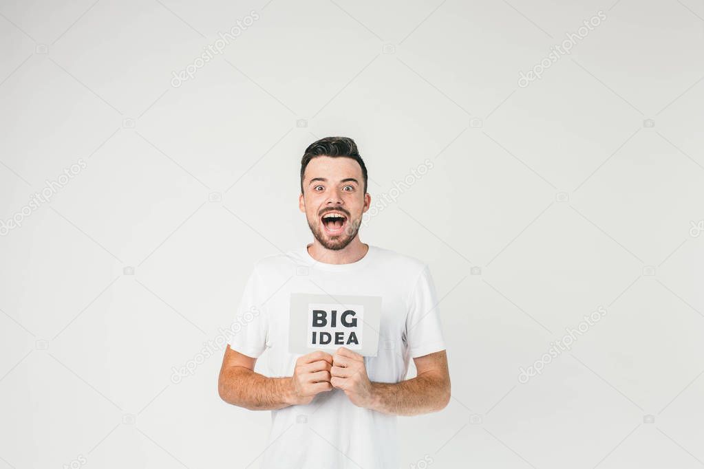 Such a beautiful photo of a young man standing in white room in white t-shirt and showing an inscription of Big Idea and he really has it, it has just come to his mind.