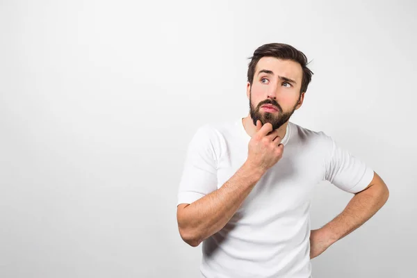 Unshaved and thoughtful guy is wearing white shirt and posing. He is keeping his right arm close to the chin and thinking. Isolated on white background — Stock Photo, Image