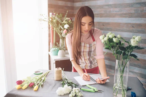 Florista femenina en el trabajo: mujer morena bastante joven haciendo ramo moderno de moda de diferentes flores. Mujeres trabajando con flores en taller — Foto de Stock