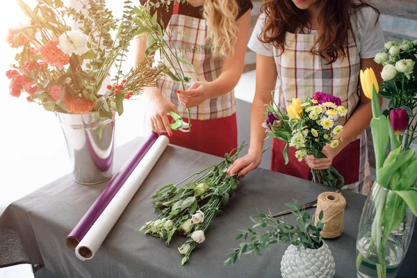 Flores entrega vista superior. Floristas creando orden, haciendo ramo de rosas en la tienda de flores. Dos floristas femeninas están haciendo ramos. Una mujer recogiendo rosas para un montón, otra chica está trabajando también . — Foto de Stock