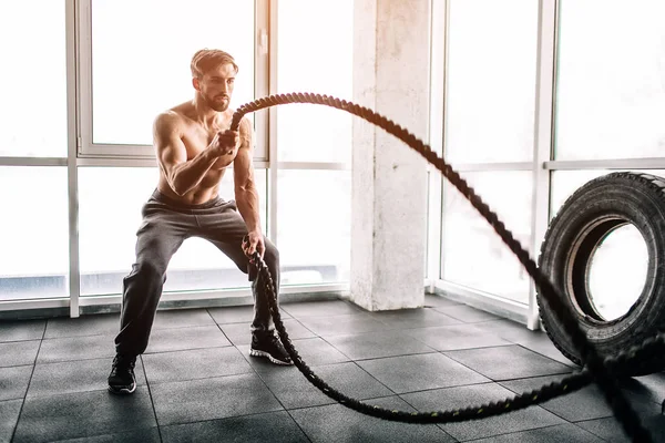 Hansome and well-built man is doing some exercises with waving two big and thick ropes one after another. This exercise is very intensive.