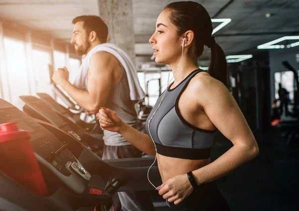 Jovem e mulher estão correndo na máquina de corrida. Eles fazem este exercício toda vez que vêm ao clube de fitness. Vista para corte . — Fotografia de Stock