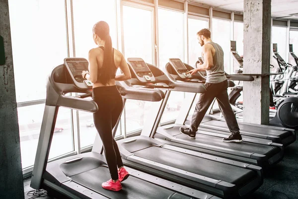 Uma pequena vista da grande sala de desporto onde duas pessoas estão a fazer exercício. Eles estão rodando em máquinas elípticas. O exercício é intenso e difícil . — Fotografia de Stock