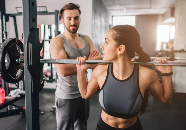 Close up van een meisje wil hebben sommige kraakpanden in Smiths machine. Ze kijkt naar haar trainer omdat ze wil hebben enige steun van hem. De man kijkt met vertrouwen naar haar student. — Stockfoto