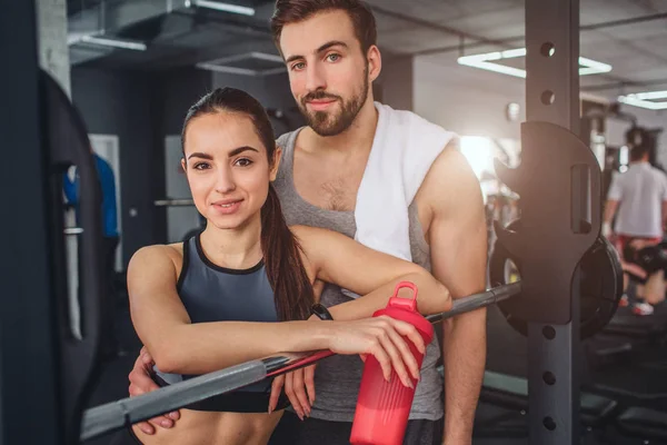 Fantástico casal está de pé juntos na sala de treinamento e posando na câmera. Ficam bem juntos. Este casal está tendo algum descanso após o treino duro . — Fotografia de Stock