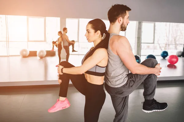 Una foto de un hombre y una mujer parados espalda con espalda y levantando una pierna. Están tratando de mantener el equilibrio de los cuerpos por una mano. De cerca. Vista de corte . — Foto de Stock