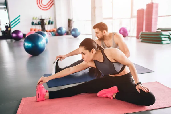 Giovani maestri dello sport sono seduti sul tappeto sportivo insieme e stretching. Si stanno riscaldando e preparando ad alcuni esercizi . — Foto Stock