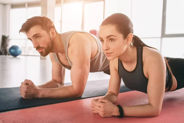 Een afbeelding vanuit een andere hoek waar twee mooie mensen zijn wokring uit en met behulp van een plank positie daarvoor. Beiden zoekt ongecompliceerd. Close-up. Geknipte weergave. — Stockfoto