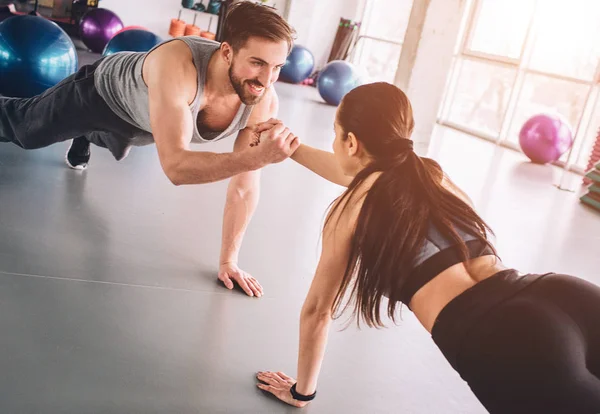 Due persone che amano il fitness sono in piedi su una mano in posizione di plancia e tenersi l'un l'altro con un'altra mano con un sorriso. La sua scena bella e adorabile . — Foto Stock