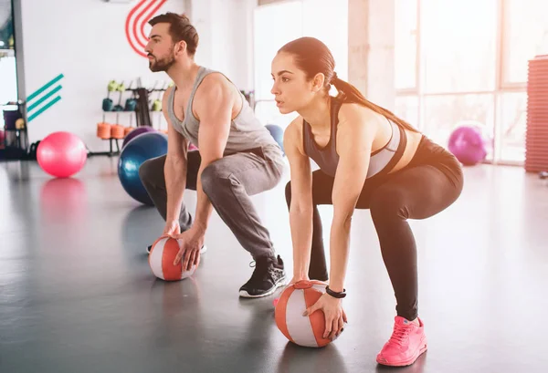 Un tipo fuerte y una chica delgada están sentados en una posición, listos para hacer sentadillas. Han puesto sus manos en las bolas listas para tomarlas y sostenerlas sobre sus manos en cualquier momento. . — Foto de Stock