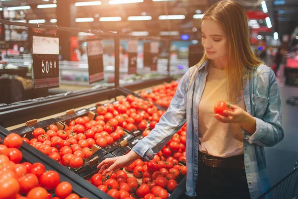 Senhora bonita e incrível está na loja grossary e escolher alguns tomates para comprar. Ela escolheu um tomate e segurou-o na mão. Fechar . — Fotografia de Stock