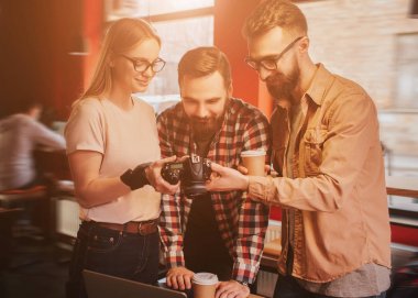 Güzel sarışın kız genç ve sakallı çocuklar n küçük bir kafe ayakta ve onları kamerada fotoğraf gösteriyor. Erkekler beğenilen sonuçtan memnun.