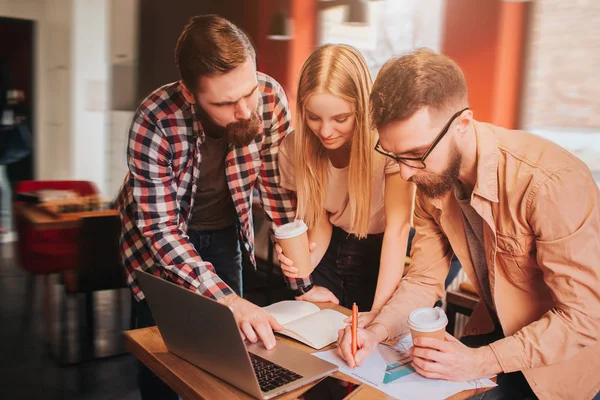 Otra imagen de tres socios comerciales que trabajan en el proyecto. Tienen la reunión en la cafetería. Chicos y chicas estudiando grafics y escribiendo la información sobre eso . — Foto de Stock