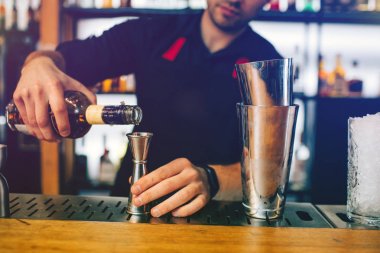 Genç barmen ölçülebilir bardağa viski yağıyor. O bir alkol kokteyl hazırlanıyor. Bu adam alkollü içecekler onun arkasında birçok botles vardır.