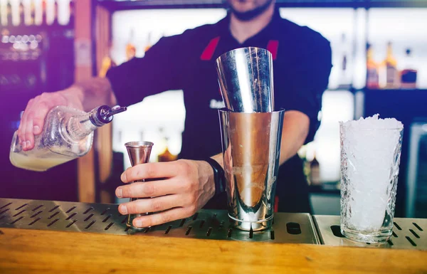 Biraz alkol küçük fincan içine ekleme ve onu tutan barmen yakın çekim. İki bardak bir başka barmans stand üzerinde duran vardır. — Stok fotoğraf