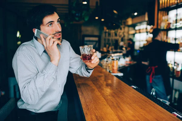 Barmans standında oturmuş ve telefonda konuşurken yakışıklı olan. Bir bardak içki ve boş zamanlarında kulüp zevk tutun. — Stok fotoğraf