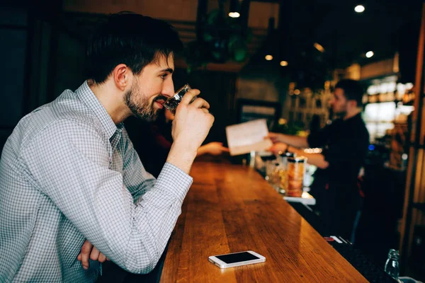 Een man zittend op de stand van de barmans en het drinken van wat alcohol uit het glas. Hij ziet er geconcentreerd. Hij lacht. Barman is het geven van een menu voor een meisje. — Stockfoto