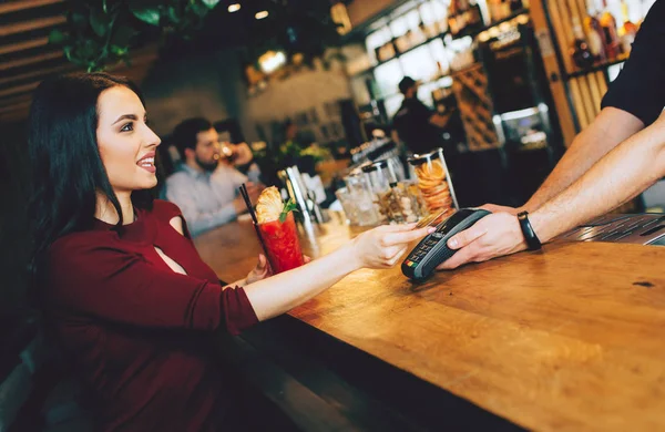 Фотография потрясающей девушки, сидящей рядом с барменом и платящей за свой заказ. Она дает бармену кредитку, чтобы заплатить за это. . — стоковое фото