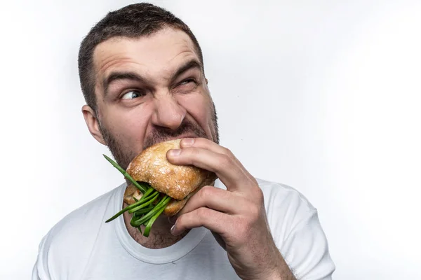 Zeer hongerig mens is het eten van een hamburger. Hij is het heel hard bijten. Ook man is op zoek ergens opzij. Geïsoleerd op witte achtergrond. — Stockfoto