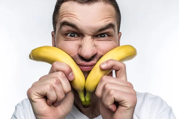 Beyaz tişörtlü bir ucube adam iki muz yüzünü yakın tutarak ve komik surat. Bu vegan meyve ve sebze yemeyi seviyor. Ayrıca inatçıdır. Beyaz arka plan üzerinde izole. — Stok fotoğraf
