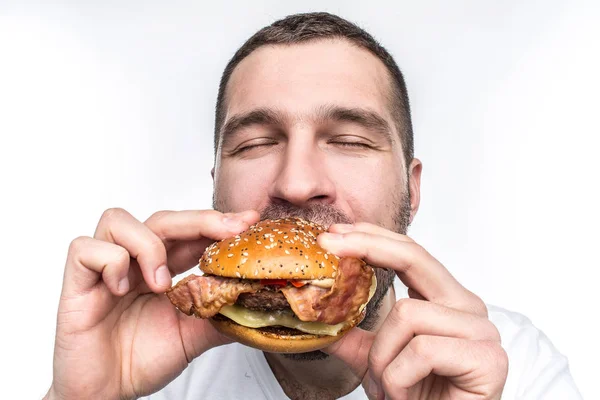 Seltsame und bizarre Mann isst fetten und saftigen Hamburger. Es ist kein gesundes Essen, aber der Kerl mag es sehr. Sein Gesicht ist sehr emotional. isoliert auf weißem Hintergrund. — Stockfoto