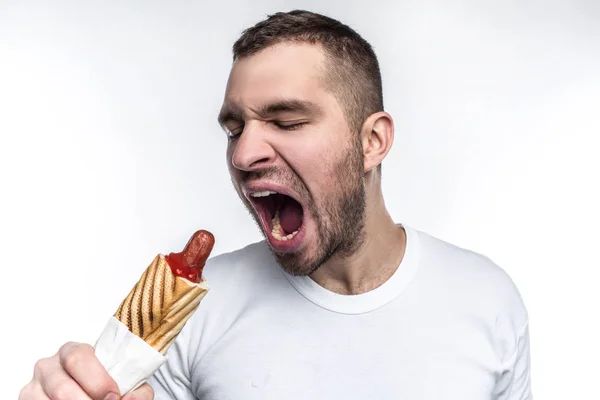 Een beeld van de man die houdt van vette fastfood. Op deze foto die hij wil bijten een groot stuk van vet hotdog. Man kijkt raar maar brutale. Geïsoleerd op witte achtergrond. — Stockfoto