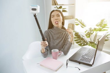 Komik genç kadın kameraya dilini gösteriyor. Blogger ve evde onu video kayıt kız.