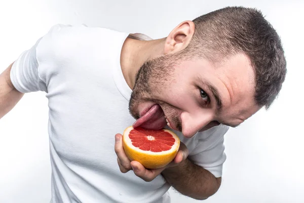 Hilarische foto van guy in wit overhemd likken de helft van de grapefruit. Hij is op zoek naar de camera op hetzelfde moment. Jongeman ziet er grappig uit. Geïsoleerd op witte achtergrond. — Stockfoto