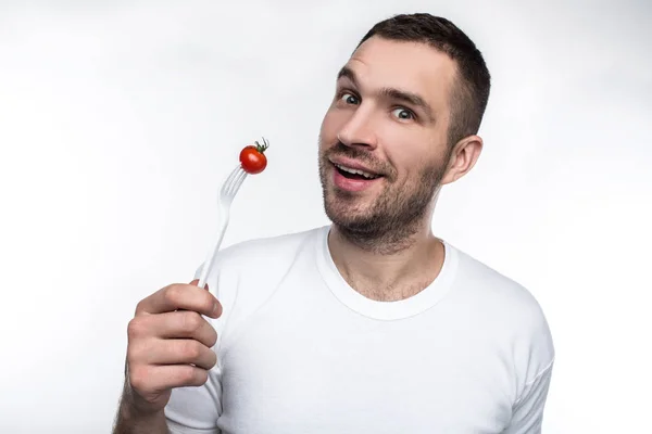포크로 작은 토마토를 먹고 잘생긴 vegeetarian의 친절 하 고 좋은 그림. 그는 맛 있는 원시 음식을 좋아한다. 흰색 배경에 고립. — 스톡 사진