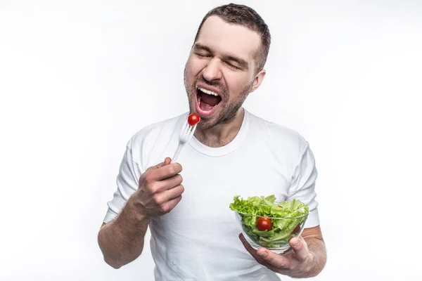 Man in een wit overhemd houdt een plaat met een groene salade en kleine tomaten in daar. Hij heeft een tomaat op de vork en klaar om te eten. Geïsoleerd op witte achtergrond. — Stockfoto