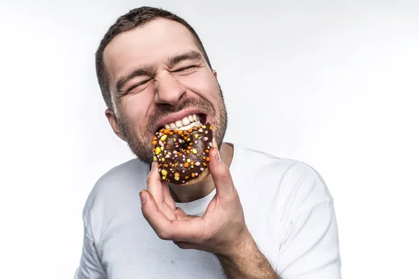 큰 사람 굶주리고. 그는 초콜릿으로 덮여 있는 작은 지방 도넛을 먹고 하기로 결정 했습니다. 그는 delisions 느낌와 기쁨 그것을 물고 있다. 흰색 배경에 고립. — 스톡 사진