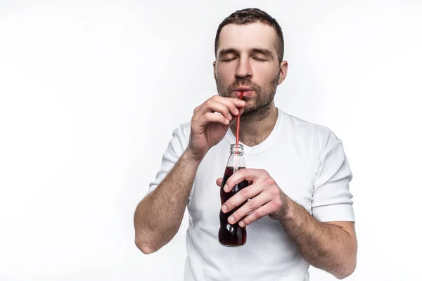 A guy with short cut is drinking coke from the bottle through straw. This man likes to eat fast food and drink sweet drinks. Isolated on white background.