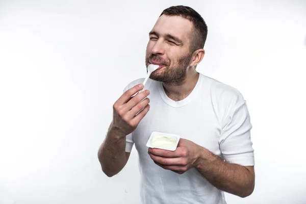 Jonge en sterke man is het eten van yoghurt. Dat doet hij met plezier. Geïsoleerd op witte achtergrond. — Stockfoto