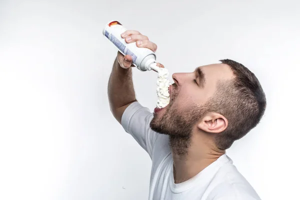 He likes sweet food among everything in a world. This man is putting some cream into his mouth with pleasure. He cant stop doing it. Isolated on white background. — Stock Photo, Image